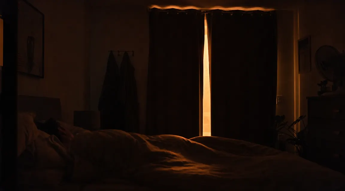 Soft bedroom at night with warm lamp light off, window showing streetlight glow through curtains, suggesting a light-leak sleep problem