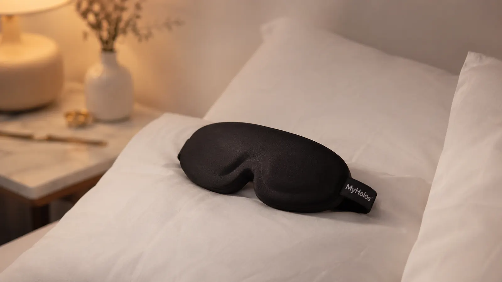 A MyHalos 3D contoured sleep mask resting on a folded white pillow in soft morning light